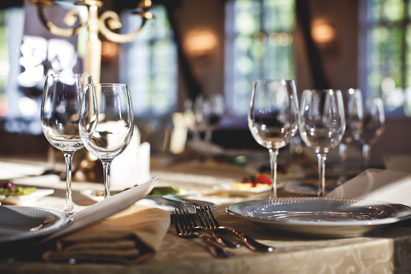 Tavola imbandita elegante: piatti, bicchieri, posate e candelabro dorato. Cena di lusso.