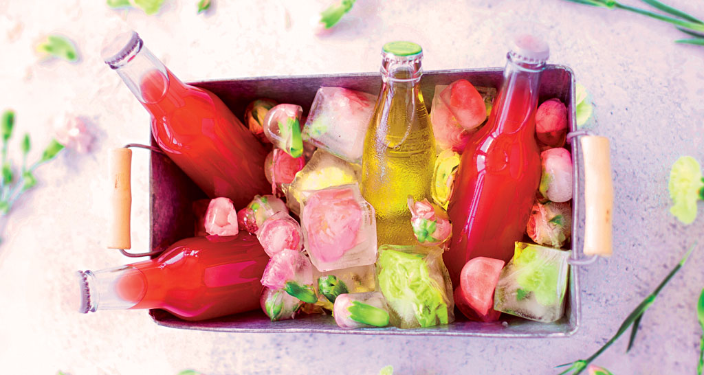 Bottiglie colorate con ghiaccio ai fiori. Bevande estive fresche.