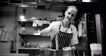 Chef in cucina. Donna con grembiule aggiunge farina. Ristorante in bianco e nero.