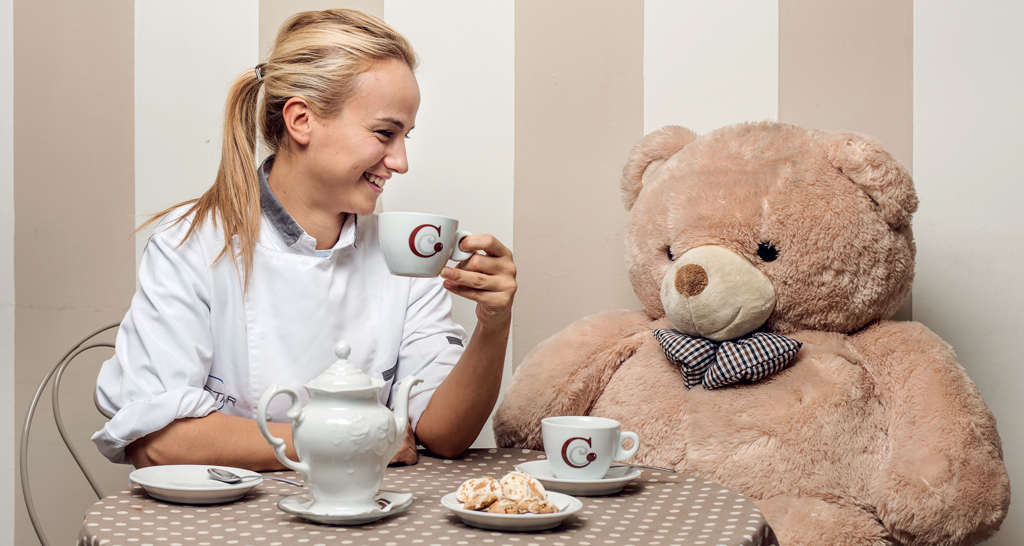 Candida Cillo con orso gigante. Chef sorridente con tazza e dolci. Pasticceria artigianale.