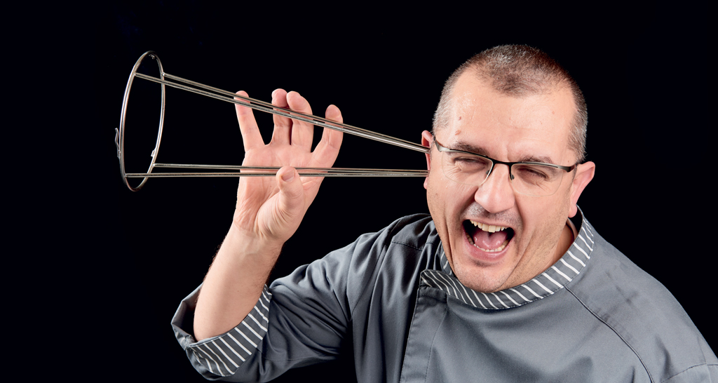 Ritratto divertente chef: uomo con utensile da cucina all'orecchio. Cucina creativa, chef italiano.