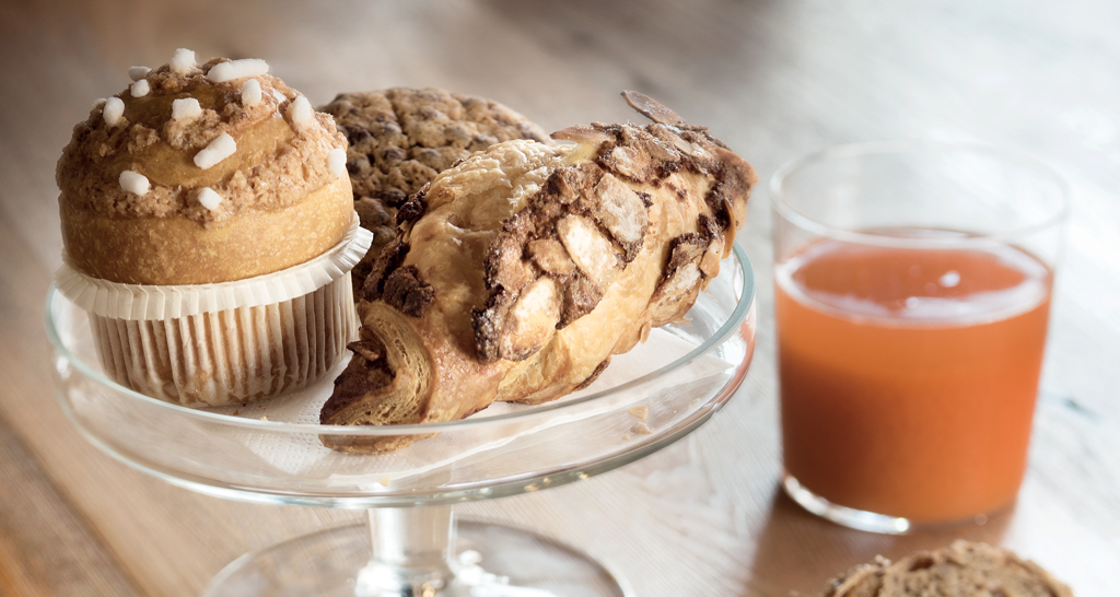 Dolci da forno su alzata: croissant mandorle, muffin e biscotto. Succo di frutta. Colazione golosa.