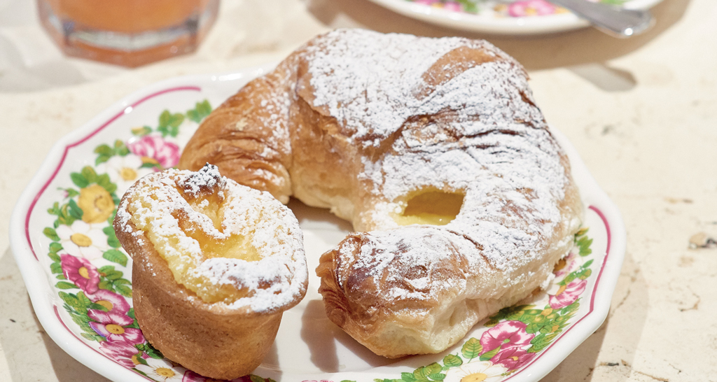 Colazione dolce: croissant e tortina con crema, spolverati di zucchero a velo su piatto decorato.