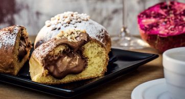 Bomboloni farciti con crema al cioccolato. Dolci italiani con zucchero a velo e granella di nocciole. Pasticceria artigianale.