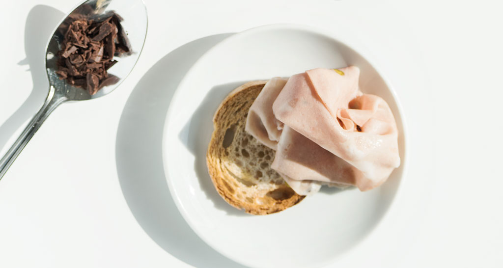 Crostone con mortadella su piatto bianco. Cucchiaio con scaglie di cioccolato. Snack gustoso.