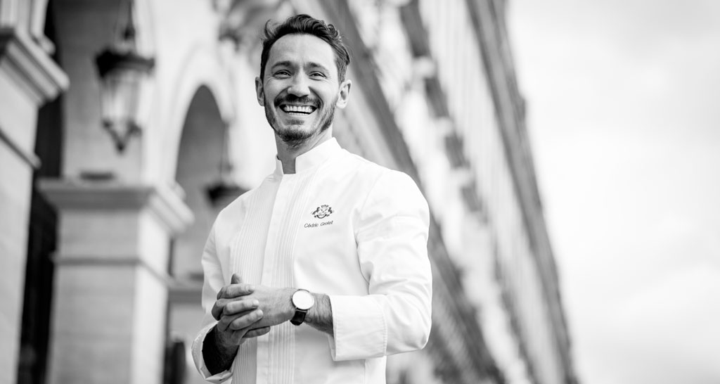 Foto in bianco e nero dello chef Cédric Grolet, sorriso smagliante e giacca da chef.