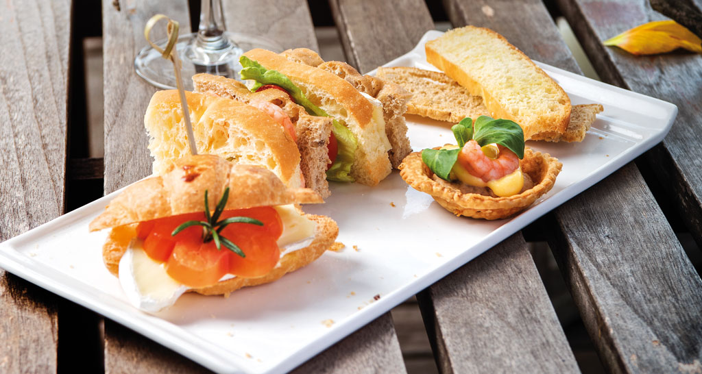 Assortimento di tartine su vassoio: croissant farcito, sandwich e tartelletta. Ideale per un brunch o aperitivo.