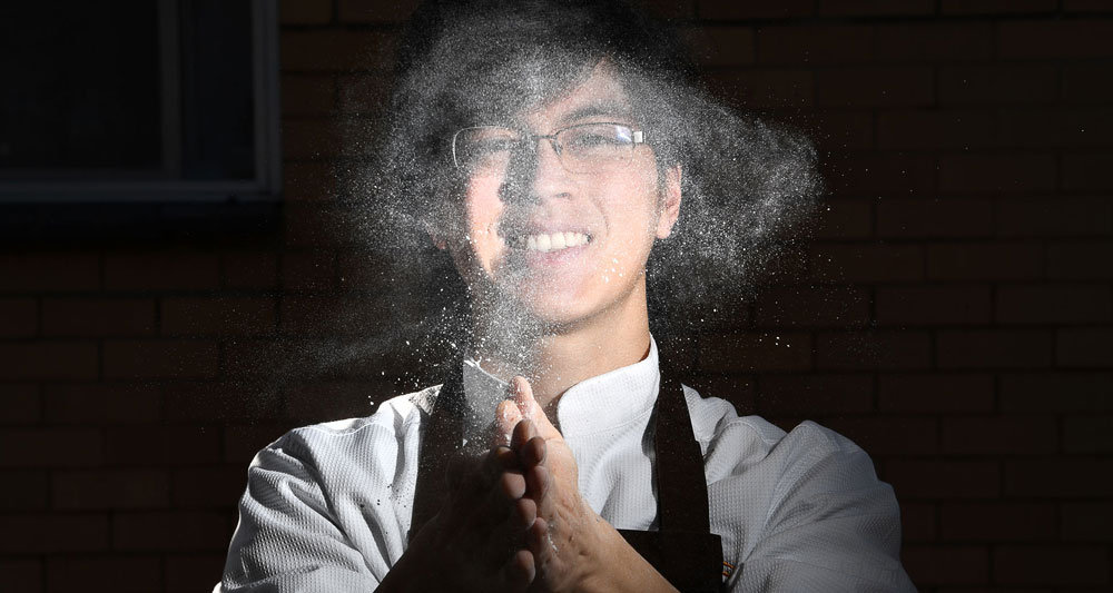 Chef pasticcere sorridente con nuvola di farina. Cucina, pasticceria artigianale, dolci fatti in casa.