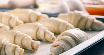 Croissant surgelati crudi su teglia. Pasta sfoglia per colazione, dolci fatti in casa.