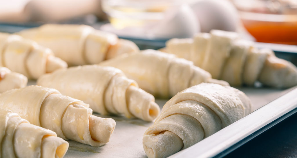 Croissant surgelati crudi su teglia. Pasta sfoglia per colazione, dolci fatti in casa.