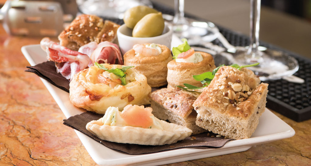 Assortimento di salatini misti su vassoio: tartine, pizzette, olive, e pasta sfoglia. Perfetto per aperitivo o buffet.