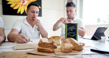 Uomini gustano pane artigianale. Farina Uniqua in tavola. Assaggio pane, prodotti da forno.