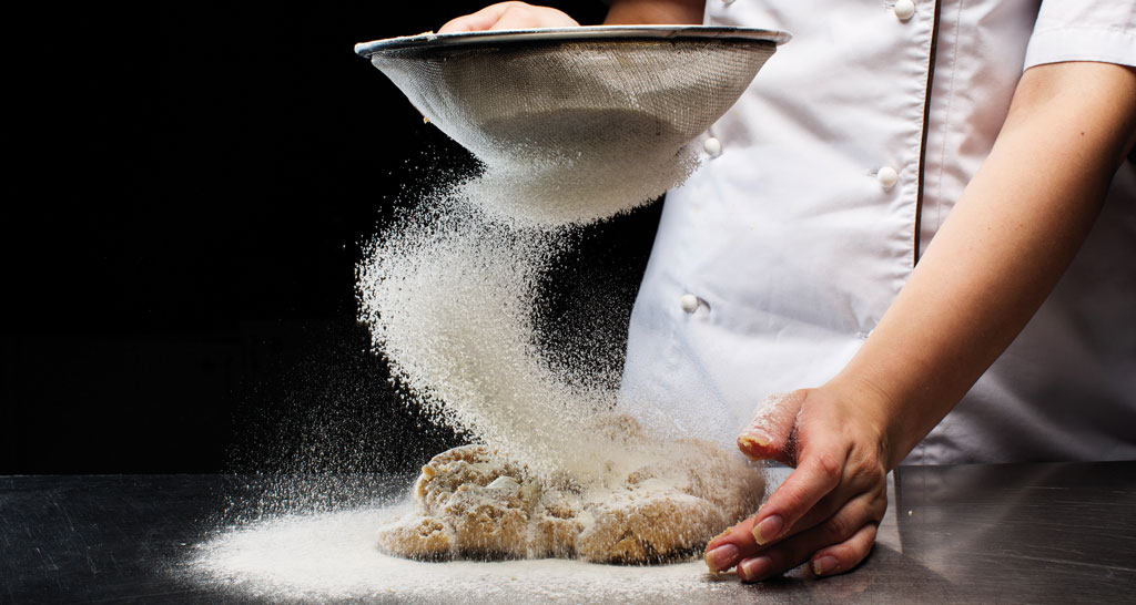 Preparazione pane: chef setaccia farina su impasto. Ricetta pane fatto in casa.