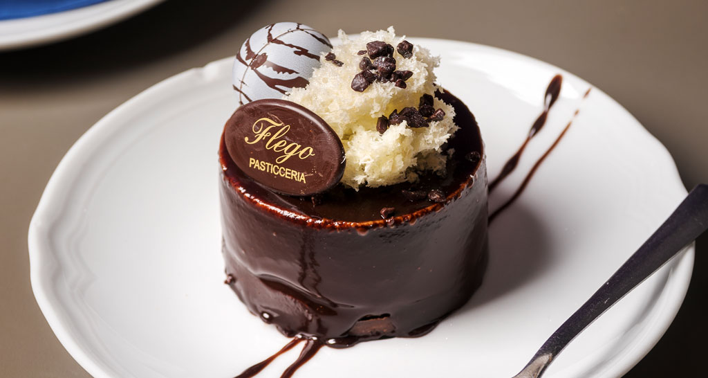 Dolce Flego Pasticceria: torta al cioccolato con decorazioni. Piatto bianco, elegante e invitante. Delizia per il palato.