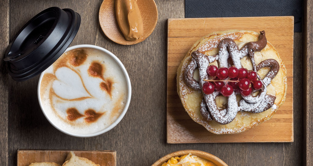Colazione golosa: pancake con cioccolato e ribes, cappuccino con latte art a forma di cuore.
