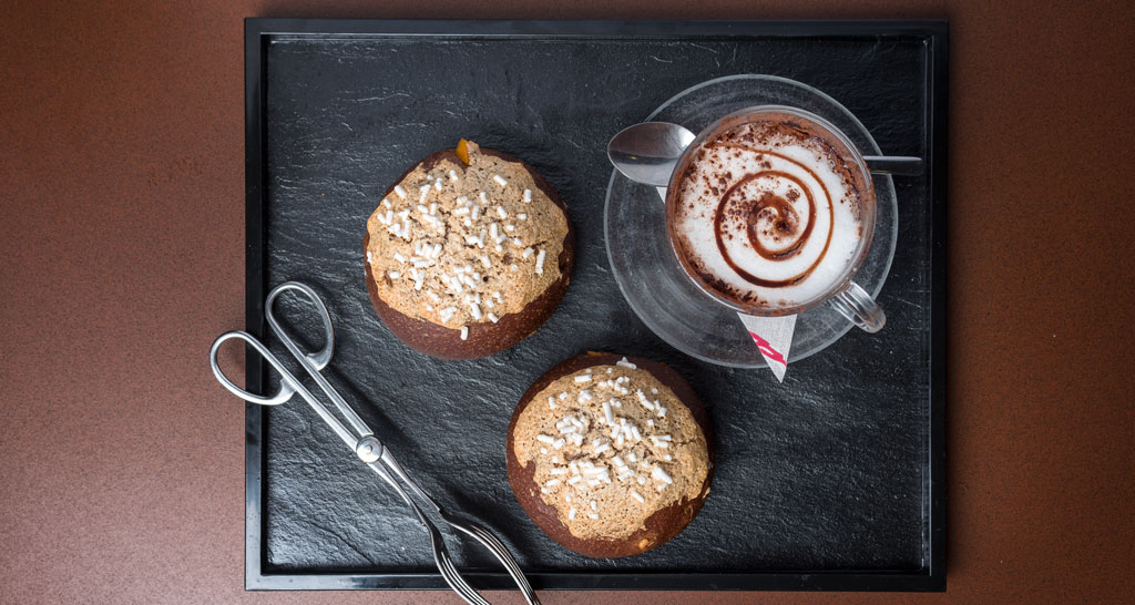 Colazione italiana: brioche con granella e cappuccino decorato su vassoio nero. Pasticceria artigianale.