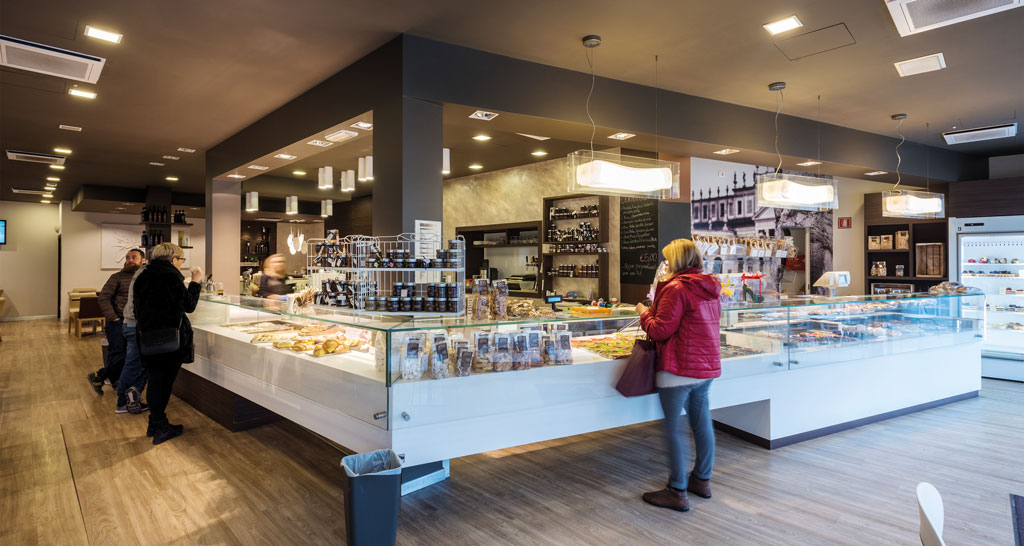 Interno di negozio alimentare: persone davanti al bancone frigo con prodotti tipici.