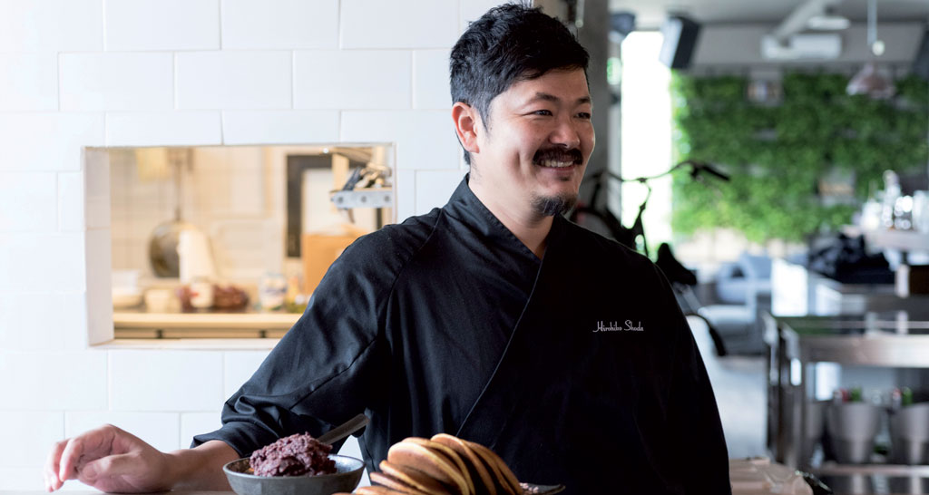 Chef sorridente in cucina con piatto di pancake. Cucina gourmet, ristorante.