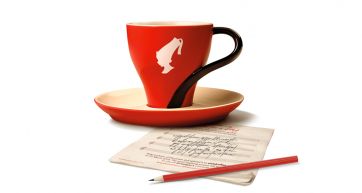 Tazza Julius Meinl rossa con logo, piattino, foglio con poesia e matita rossa.