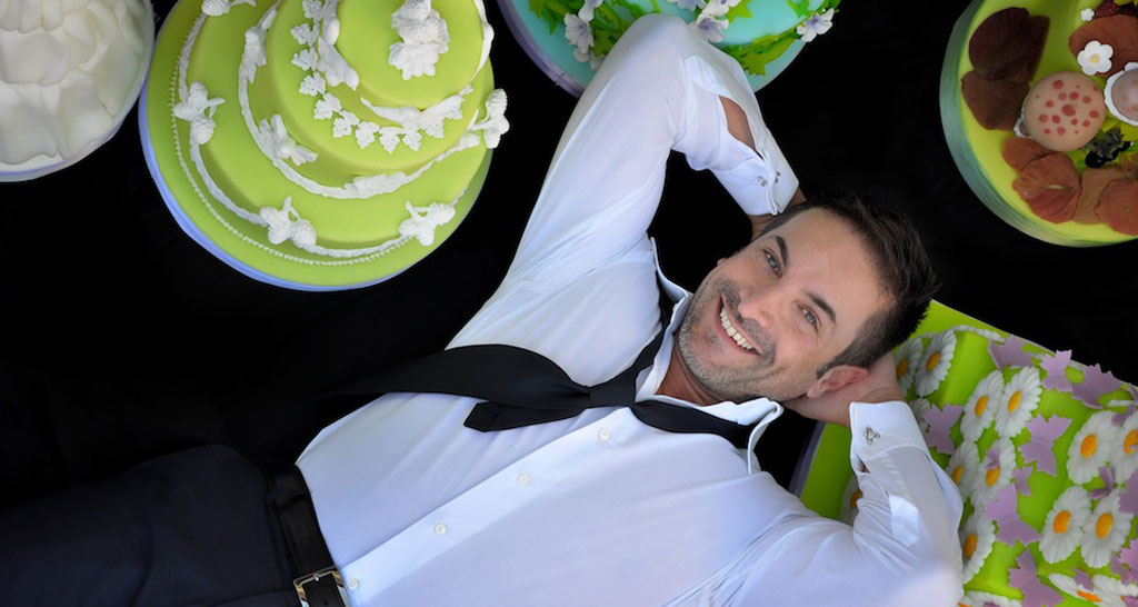 Renato Ardovino sorride, circondato da torte decorate. Cake designer, dolci artistici.