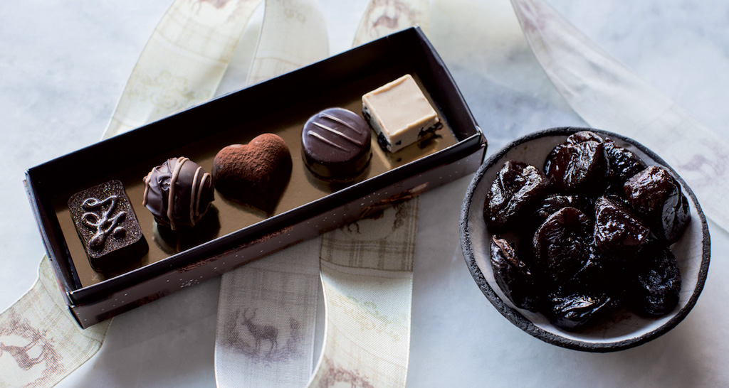 Cioccolatini assortiti in scatola e prugne secche in ciotola. Dolci prelibati.