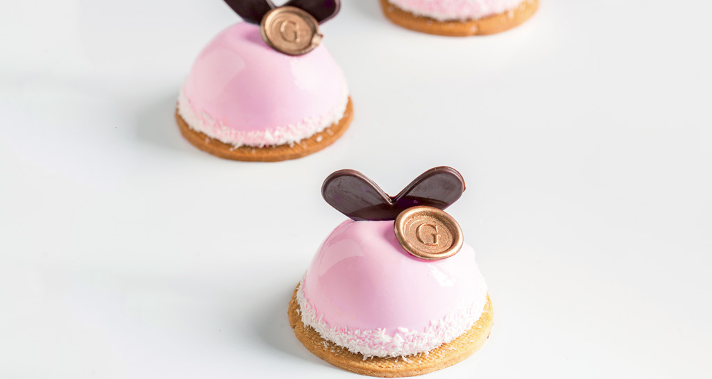 Dolci monoporzione rosa con glassa lucida e decorazioni in cioccolato. Pasticceria artigianale.