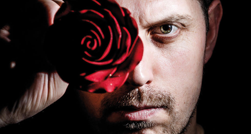 Uomo con rosa rossa. Ritratto artistico, sguardo intenso, fiore, bellezza.