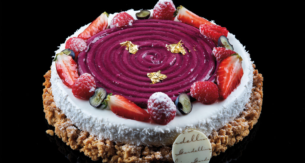 Torta di frutta fresca: fragole, lamponi e mirtilli. Dessert goloso con crema viola e decorazioni dorate.