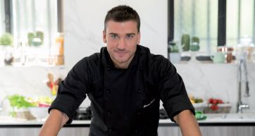 Chef sorridente in cucina. Abbigliamento da cuoco nero. Cucina moderna e luminosa.