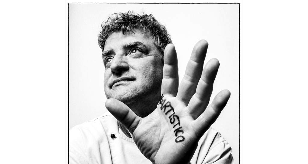 Ritratto di Mauro Morandin, chef pasticcere. Mano con scritta Artistico. Foto in bianco e nero.