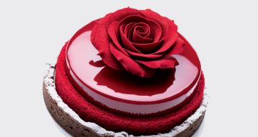 Torta elegante con glassa rossa lucida e rosa decorativa. Pasticceria raffinata.