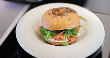 Bagel con salmone, rucola e formaggio cremoso su piatto bianco. Colazione gustosa.