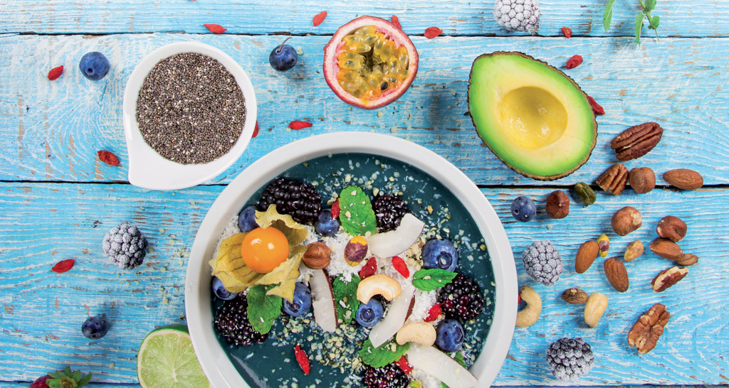 Bowl di smoothie con frutta fresca, avocado e semi di chia su sfondo di legno azzurro. Cibo sano.