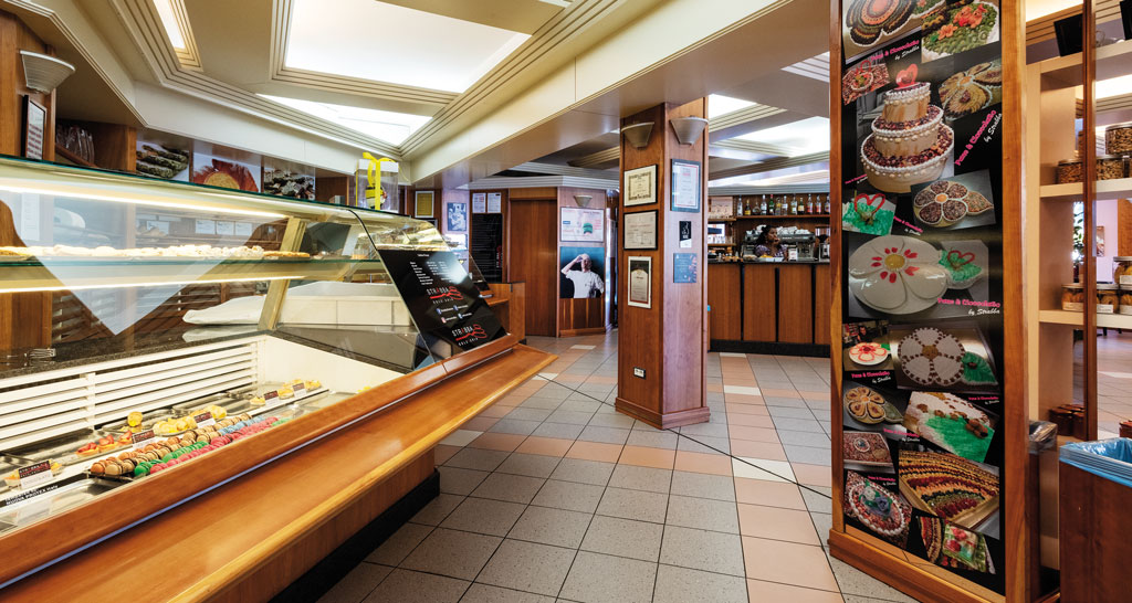 Interno di pasticceria artigianale. Vetrina dolci, banco bar in legno, foto torte decorate.