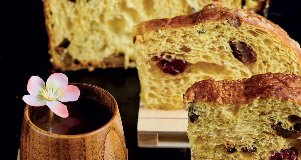 Fette di panettone artigianale con uvetta e canditi, bevanda calda e fiore. Dolce natalizio italiano.