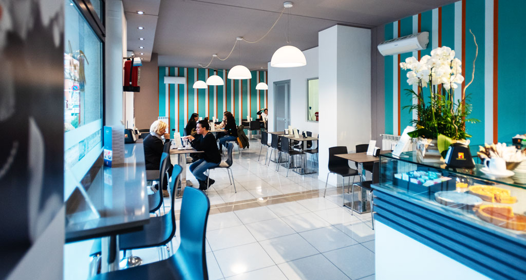 Interno luminoso di caffetteria con persone sedute ai tavoli. Arredamento moderno, pareti a righe.