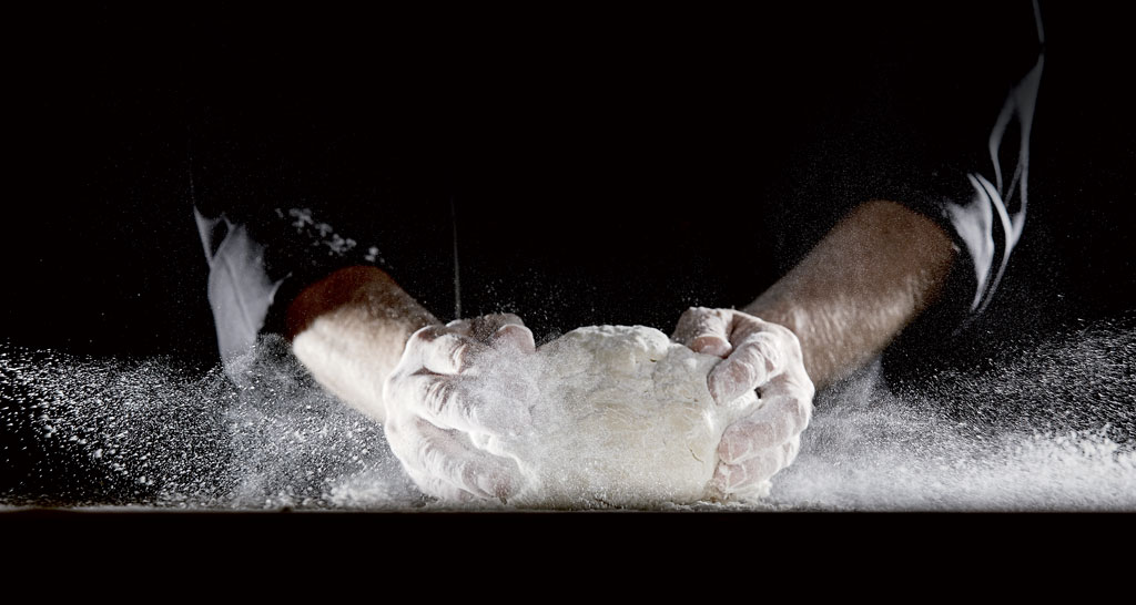 Impasto con farina. Mani che lavorano la pasta, nuvola di farina bianca. Ricetta pane fatto in casa.