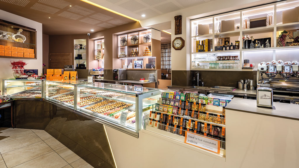 Interno di pasticceria artigianale con vetrine di dolci, cioccolatini e scaffali illuminati. Design elegante e accogliente.