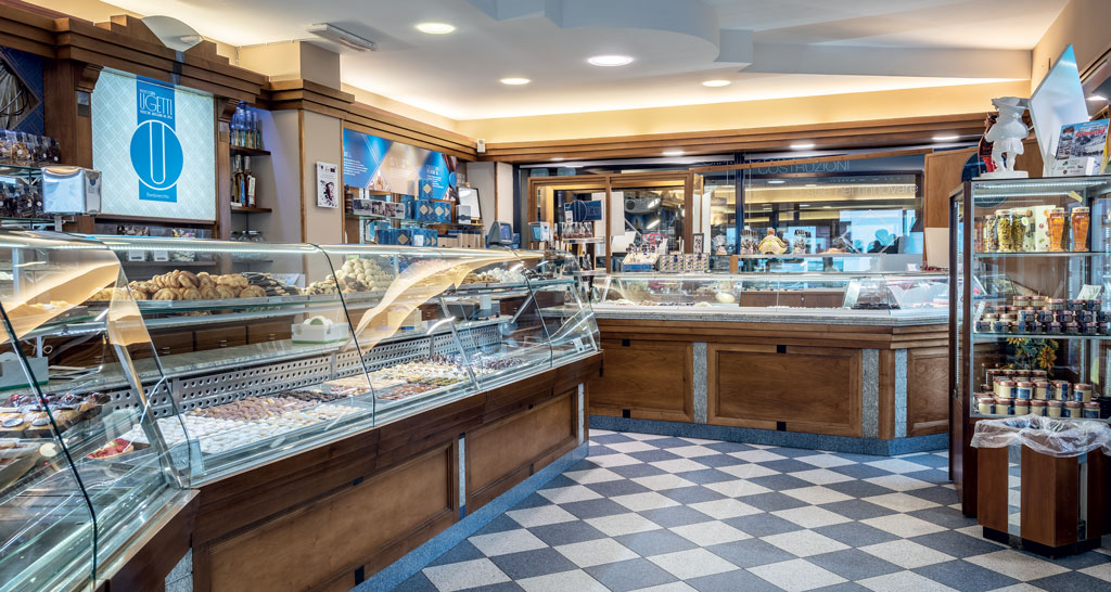 Interno pasticceria Ugetti: vetrine con dolci, cioccolatini e biscotti artigianali. Pavimento a scacchi.