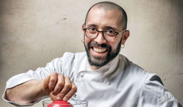 Chef sorridente in divisa bianca con pomodoro. Cucina italiana.