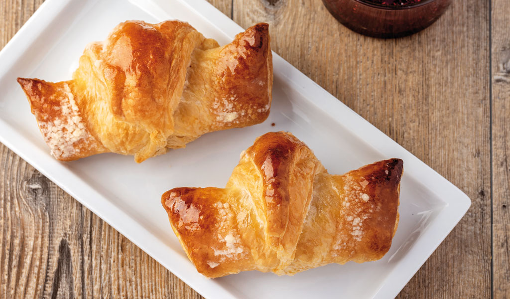 Due croissant dorati su piatto bianco. Colazione dolce, pasticceria italiana.