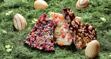 Cioccolato artigianale di Pasqua su erba: uova decorate e tavolette con frutta secca. Delizie pasquali, dolci golosi.