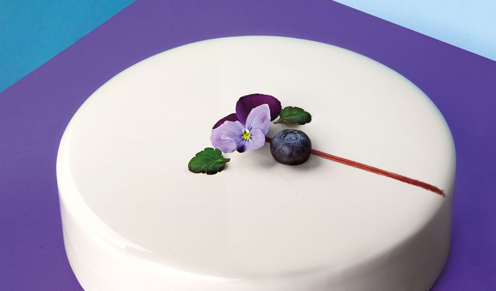 Torta moderna bianca con fiore viola e mirtillo. Pasticceria creativa, dessert elegante.