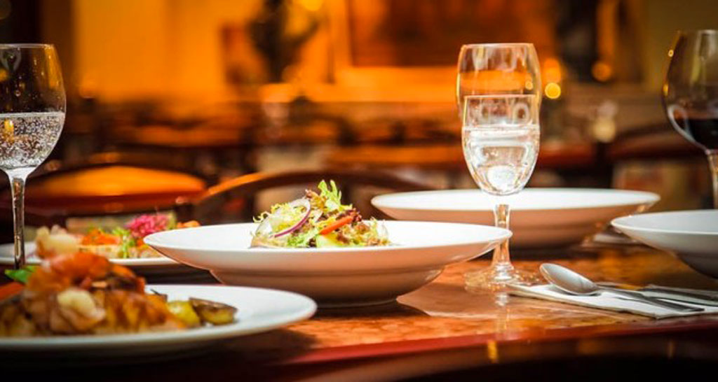 Tavola imbandita con piatti gourmet, insalata e bicchieri. Ristorante, alimentazione fuori casa.