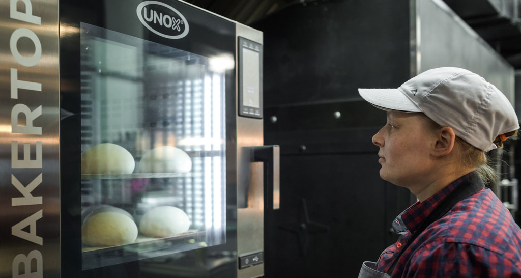 Donna guarda forno BAKERTOP Unox con pane. Attrezzatura professionale per panetteria e pasticceria.