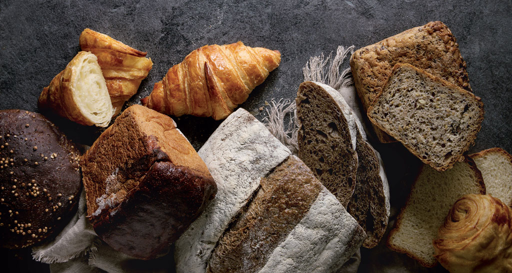 Assortimento di pane artigianale: croissant, pane integrale, segale e lievito madre. Panificazione varia e gustosa.