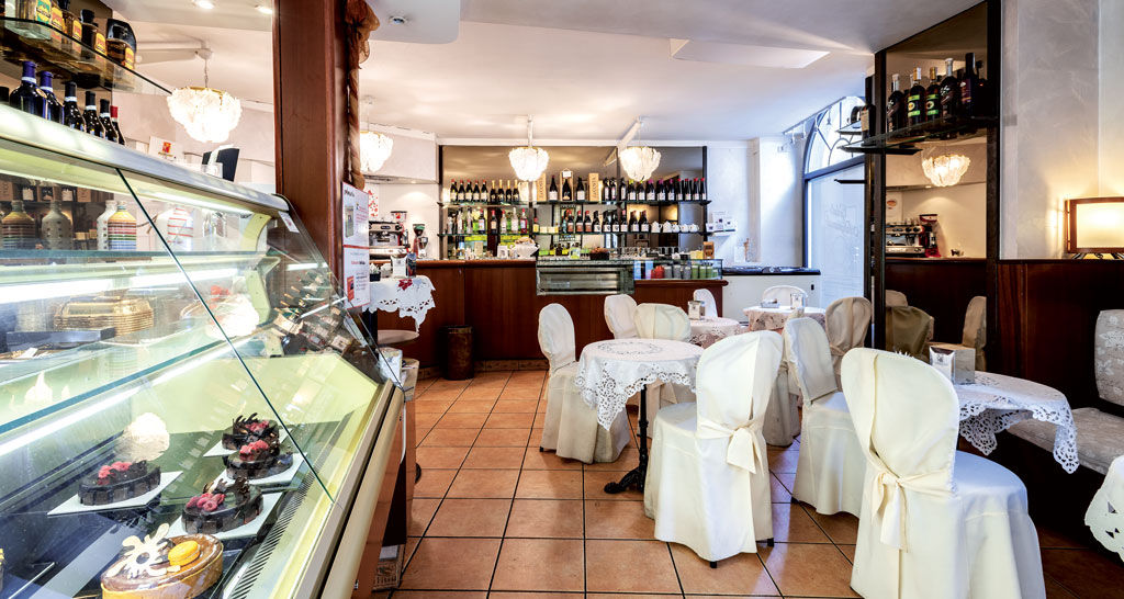 Interno accogliente di pasticceria italiana con vetrina di dolci e tavolini eleganti.