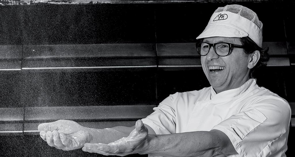 Chef sorridente cosparge farina. Artigiano panettiere al lavoro.