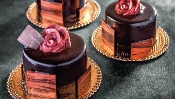 Pasticcini al cioccolato con decorazione a rosa. Dolci artigianali su piatti dorati.