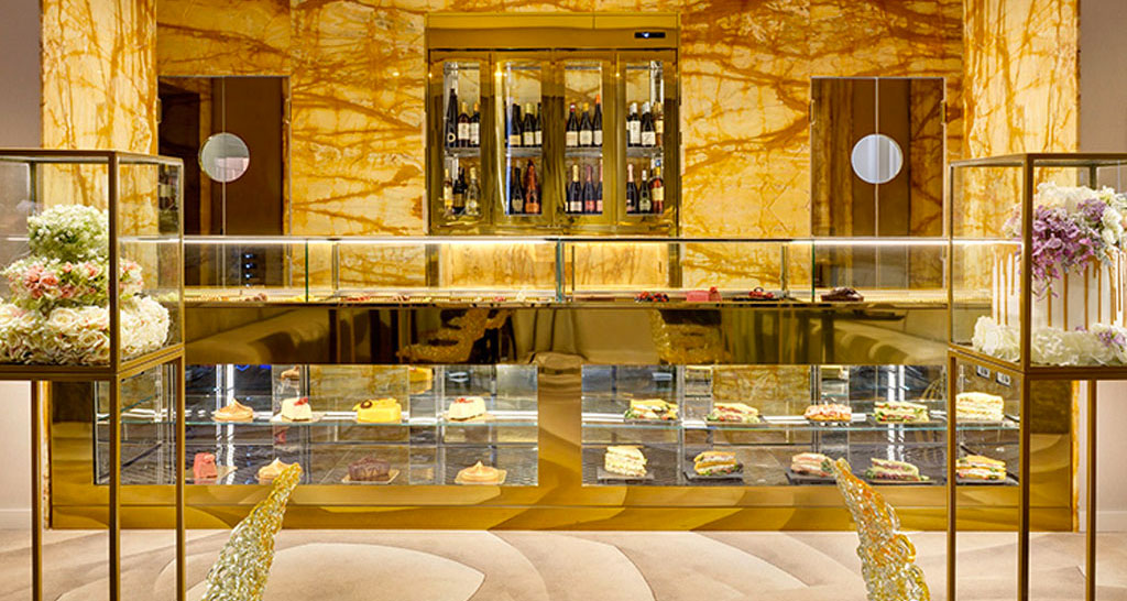 Elegante pasticceria hotel: vetrine dorate con torte, pasticcini e vini pregiati. Design lussuoso, marmo e fiori.